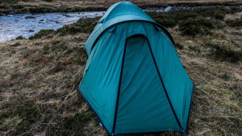 a blue lightweight thru hiking tent pitched near a lake