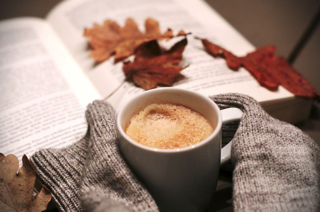 Cup of coffee with a book and autumn leaves, highlighting the serenity of fall camping.