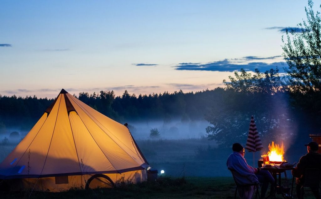 A cozy evening scene with an older couple dining by a campfire next to their portable glamping tent.