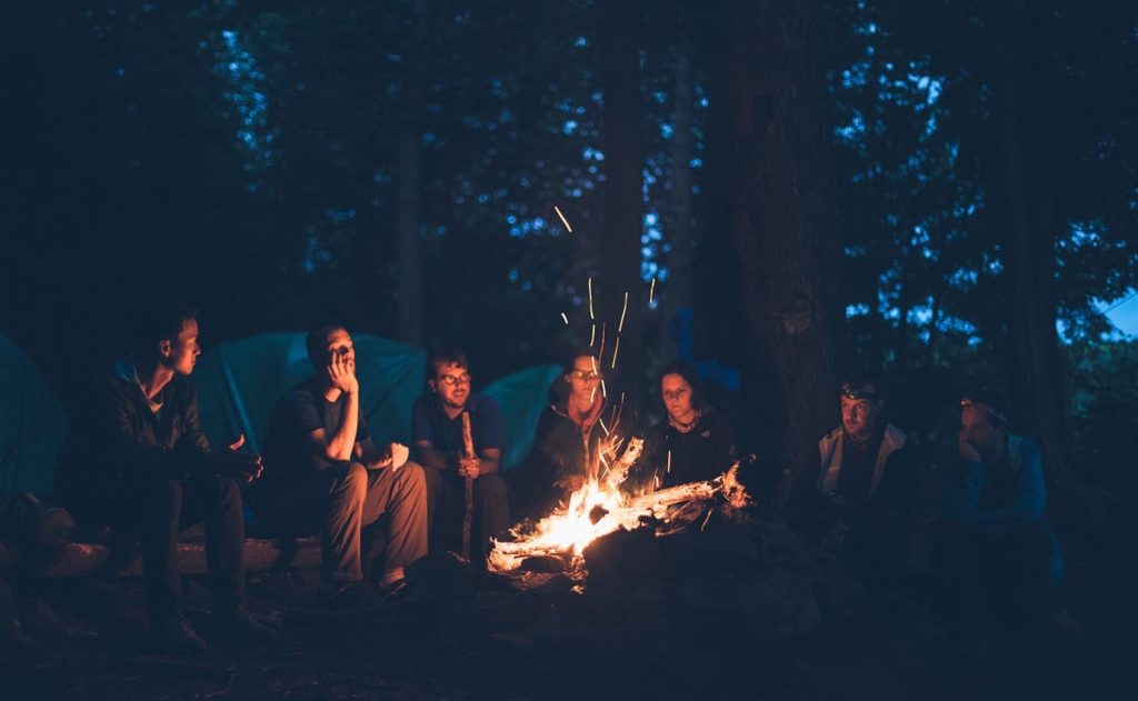 A group of seven friends by a campfire at night waiting to see who will begin telling campfire stories.