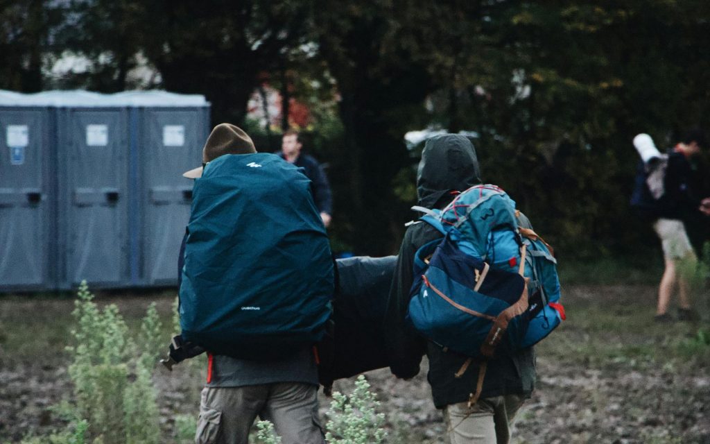 Two kids with backpacks working together to carry a tent for setup.