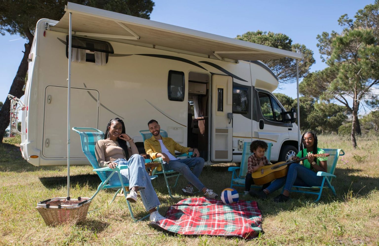 Husband, wife and two children sitting under an RV awning for a day of family camping.