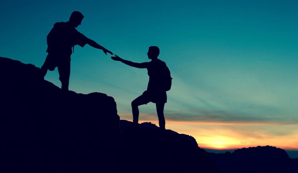 Father helping son on a mountain at sunset by reaching out hand for assistance.