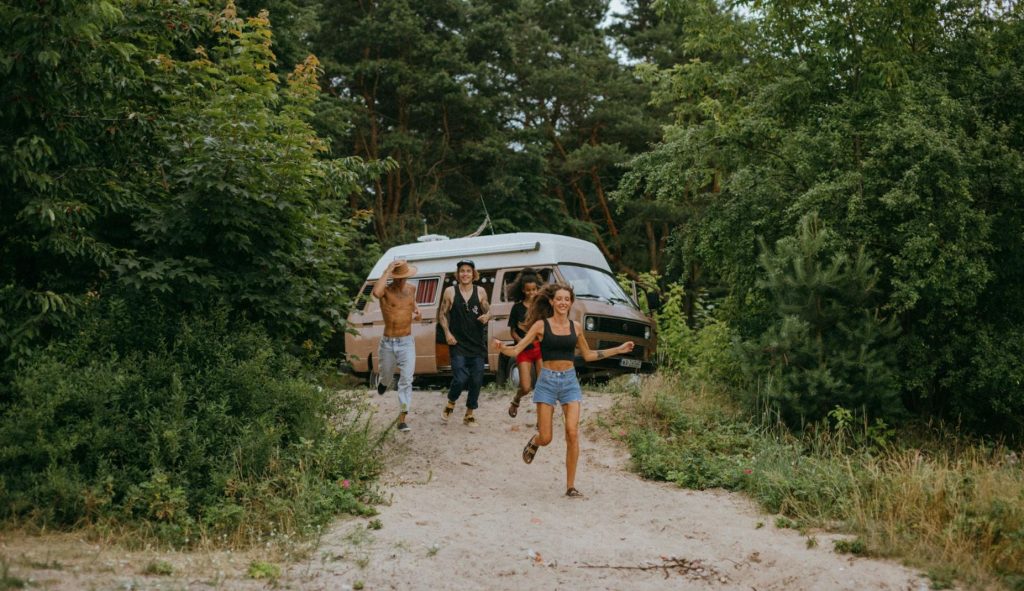 4 friends leaving their camper van in a secluded place, running down a hill for a day of fun.