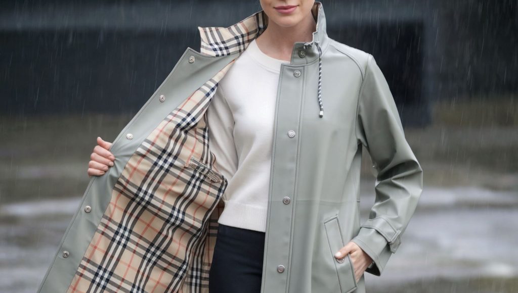 Woman wearing a stylish glamping raincoat, light sea mist green with tan, black, and red plaid interior.