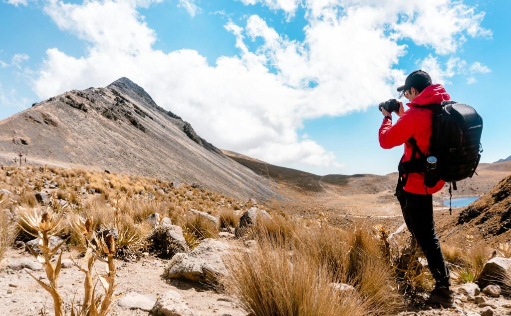 Backpacker taking a photo of an arid mountain/desert landscape on the left with a lake to the right.