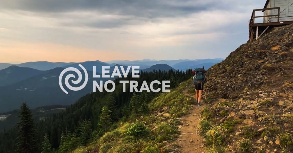 Hiker walking along a mountain ridge with a spectacular view. The Leave No Trace Center for Outdoor Ethics logo appears in text overlay.