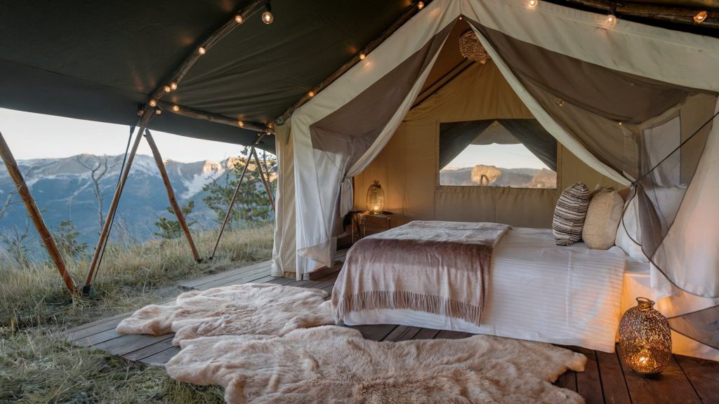 A cozy mountaintop glamping tent with warm rugs, luxury furnishings and stunning views of the snowcapped mountains in the distance.