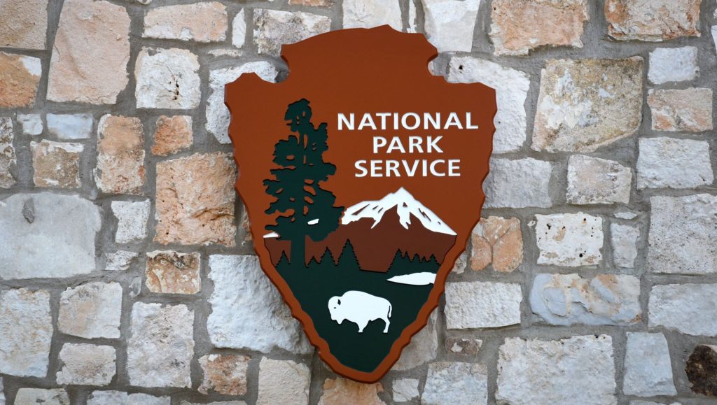 The National Park Service Logo carved in wood and mountain on a stone wall.