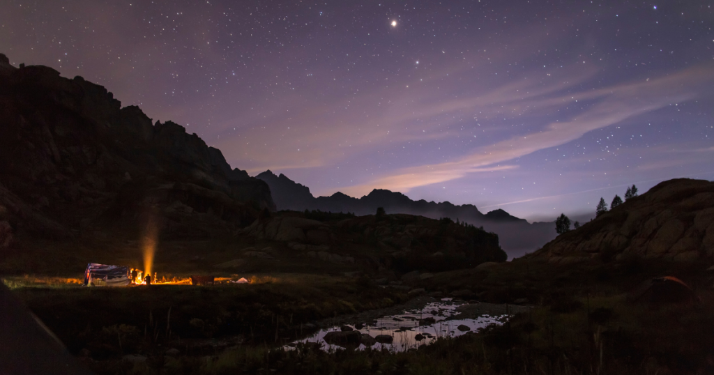 A family cooking by a fire at night in a remote location by a river.