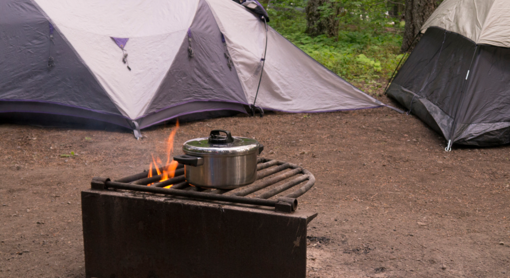 Single pot on a campfire grill next to two tents.