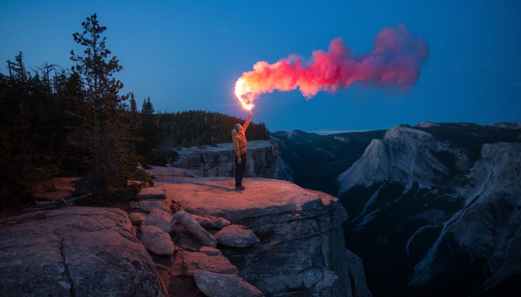 Hiker on a mountain ridge using a signal flare to indicate distress, a key piece of camping gear as well as an important camping skill to have.