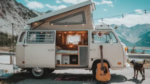 VW camper van in a parking area amid a mountain backdrop with a dog and guitar in the foreground.