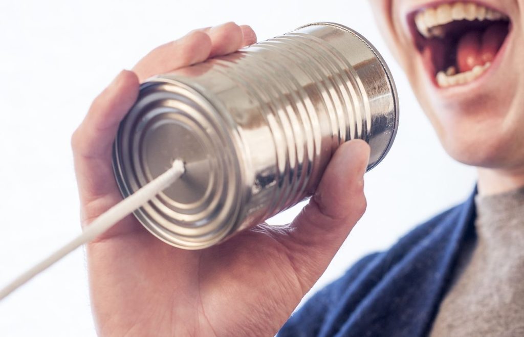 Man raising his voice into a tin can to show the power of voice in campfire storytelling.