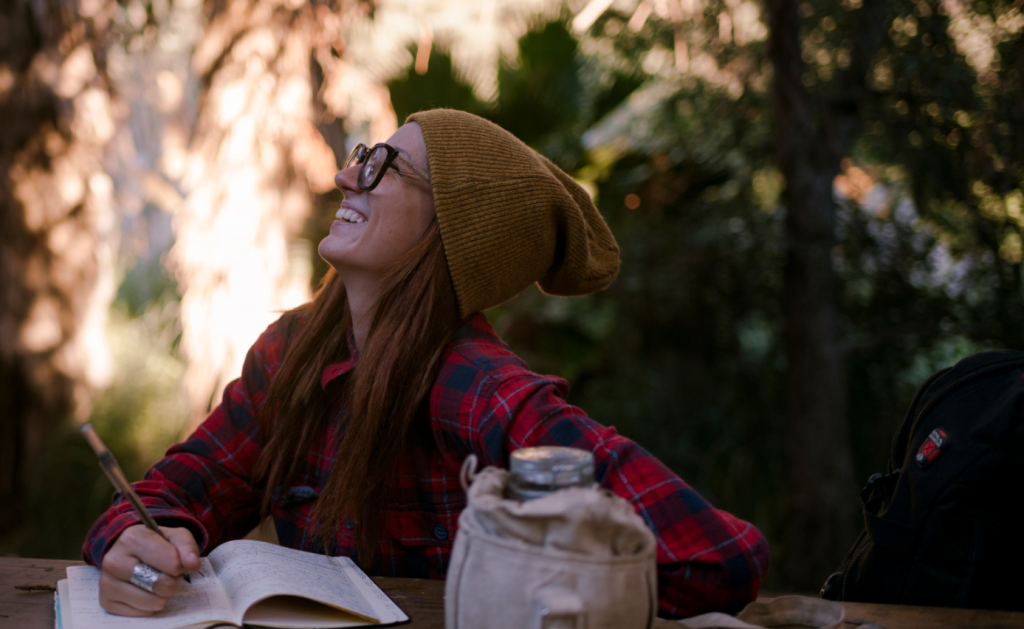 A woman is admiring nature at a picnic table and journaling what she sees - one of the many free forms of entertainment for the van life.