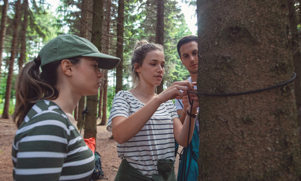 Three campers learning the basic skills of setting up a survival shelter while camping in the wilderness. 