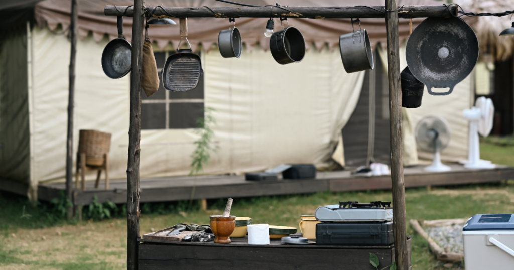 A campsite filled with essential camping utensils for a campfire cook kit: spatula, tongs, pots, knives, cutting board and more.