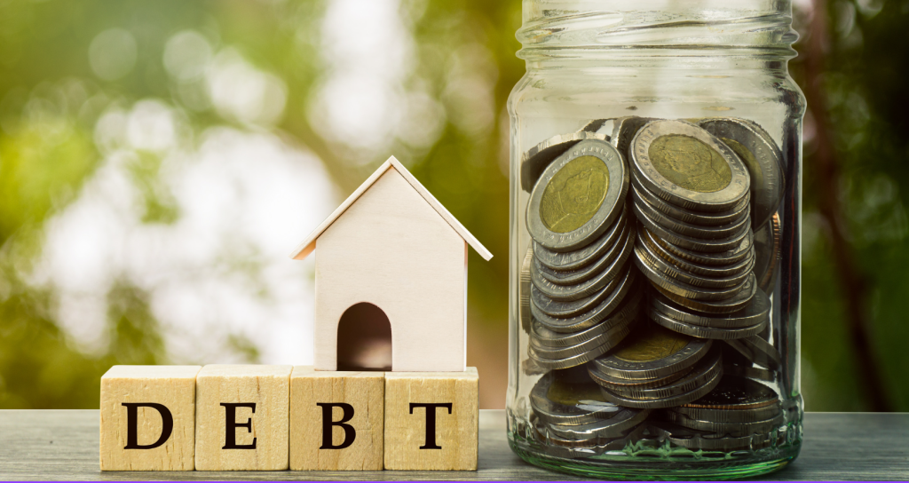 Debt is spelled out with blocks beneath a model of a house on the left, and on the right is a jar full of coins to highlight saving money with van life on the road.