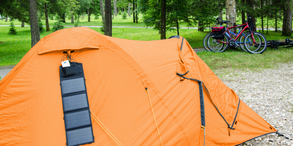 An orange tent in a park-like campsite with a hanging foldable solar panel.