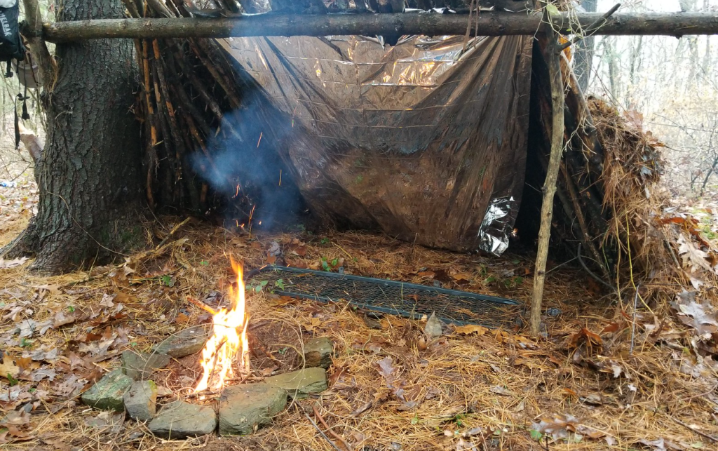 An improvised lean to shelter for survival with campfire.