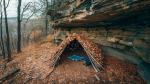 A survival shelter made with branches and leaves near a cliff wall to use for wind protection in autumn.