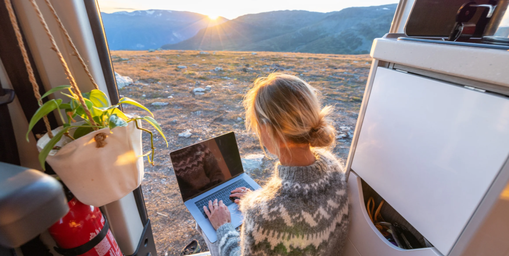 A woman working on a laptop during a beautiful sunrise over the mountains. There are many options for van life people to make money.