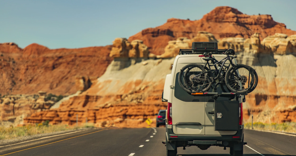 The back of a van heading down a picturesque road in Arizona with 2 bicycles on the back.