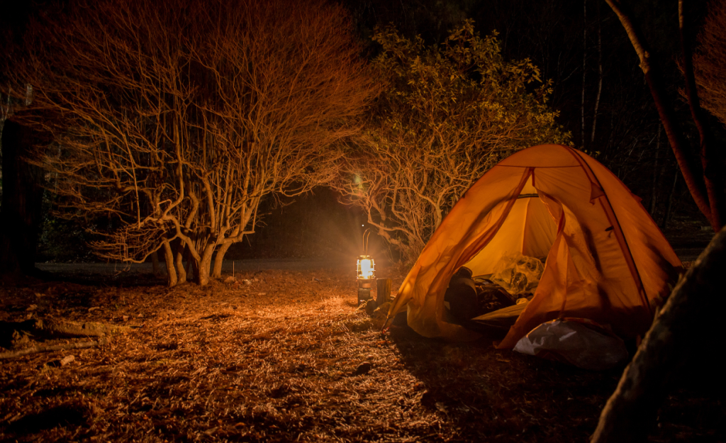 A camping lantern illuminates a campsite at night.