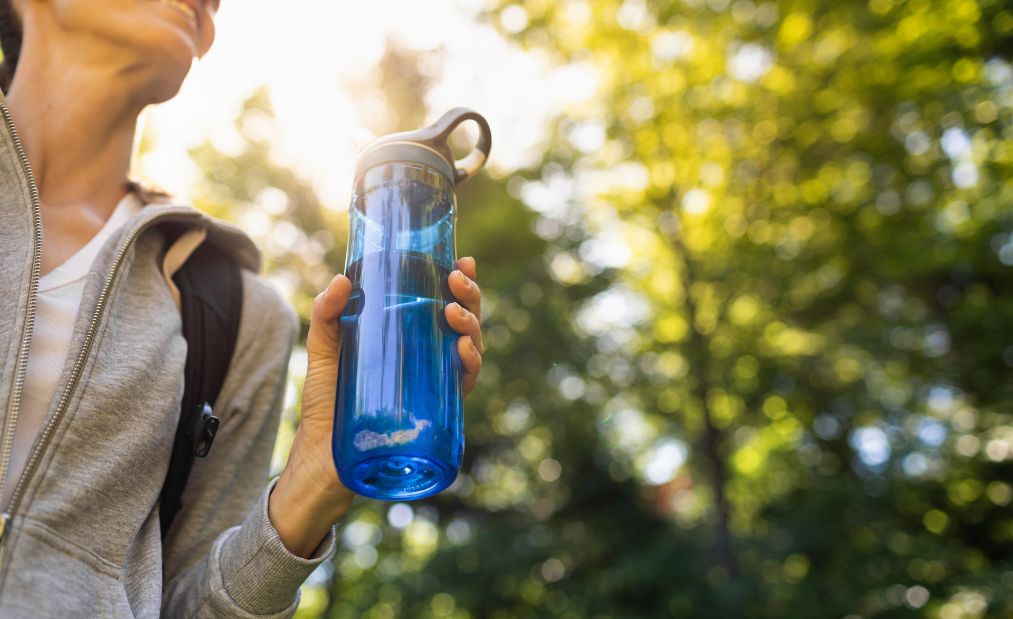 A woman holding a lightweight water bottle while hiking in the forest.