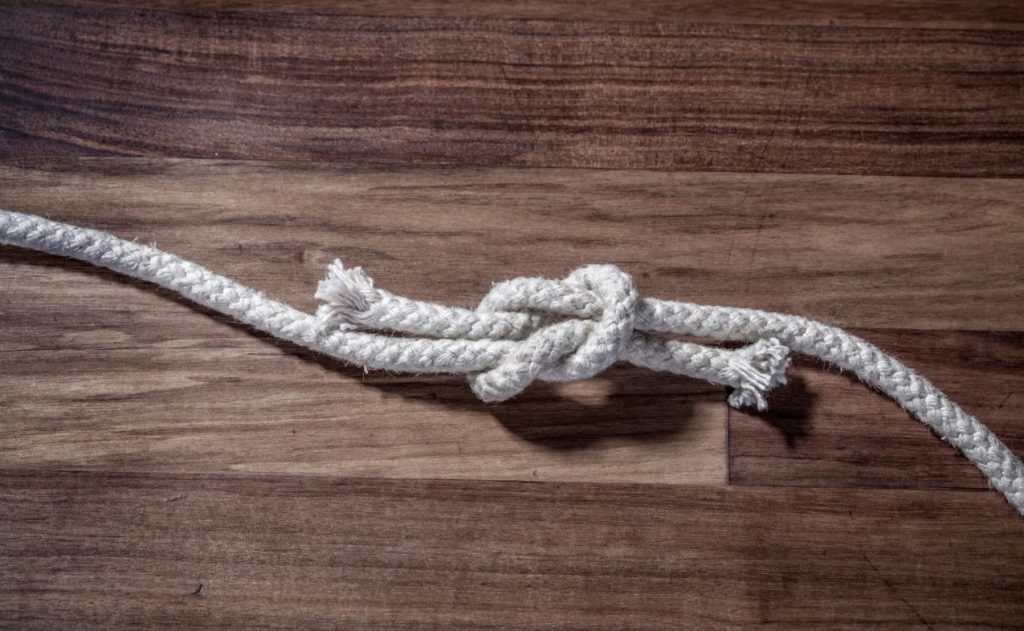 A square knot of white rope on a dark wood background.