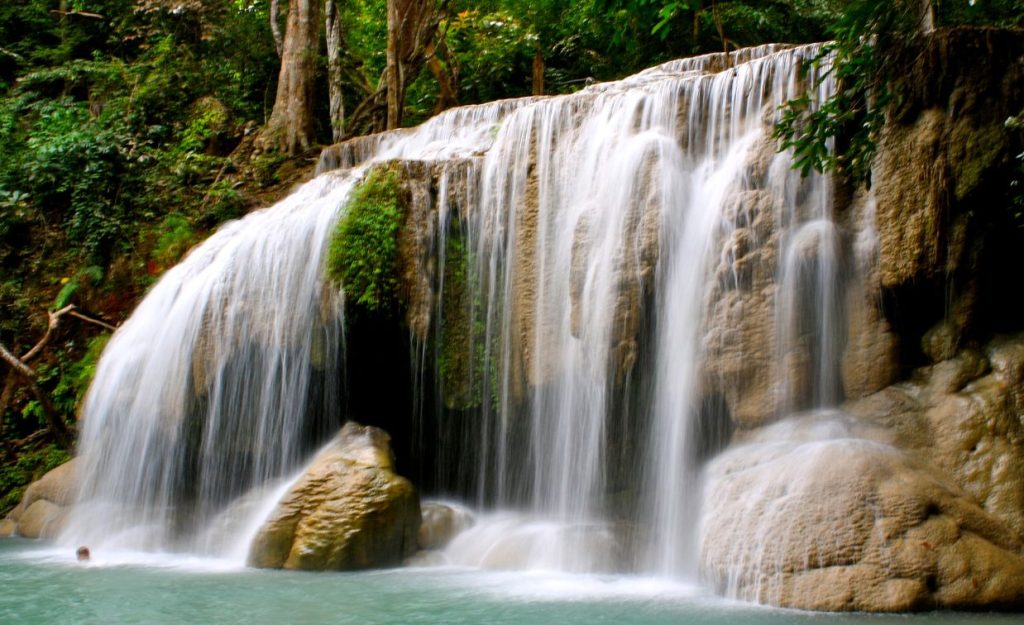 The emerald waters of Erawan Falls in Thailand with the water cascading from the rocks above.