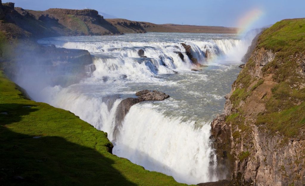 The incredible Gullfoss falls in Iceland, showing the scope and power. A small rainbow is seen in the upper right amid the rocky landscape.