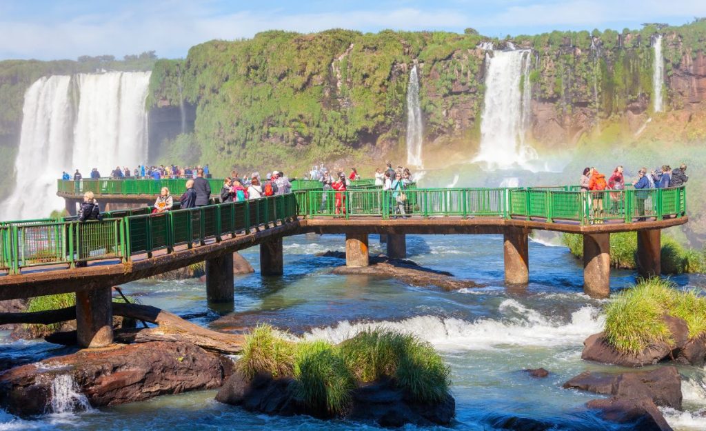 Tourists standing on a fenced-in pier in front of Iguazu Falls, Argentina.