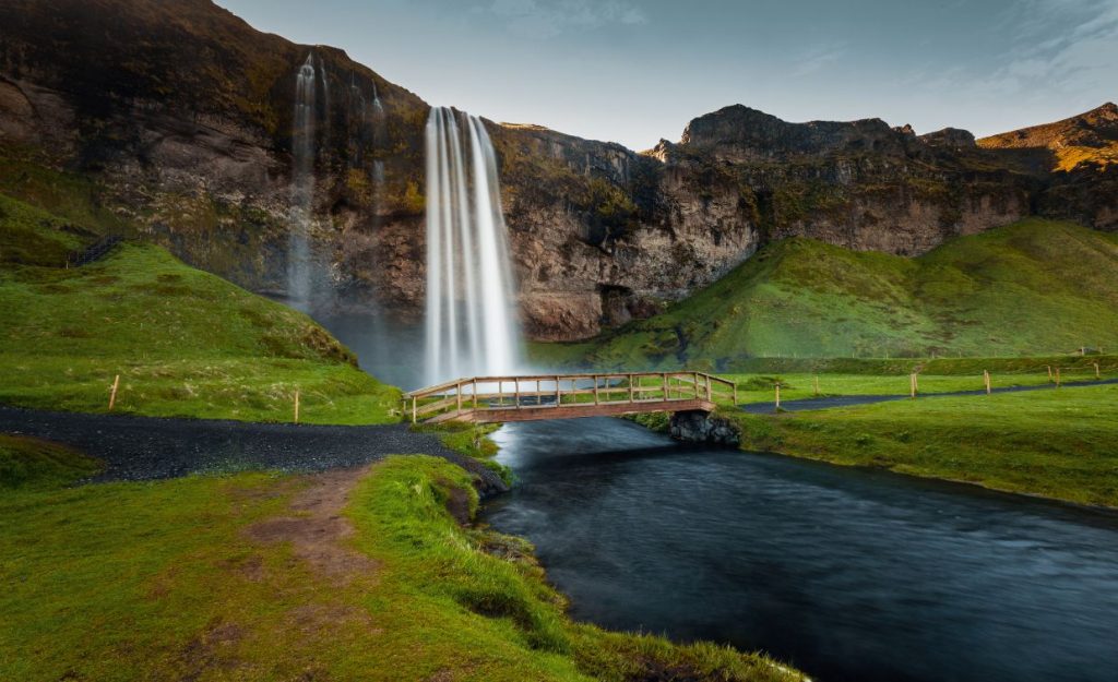 Seljalandsfoss seen from the ground in front of a walking bridge in front of the falls.