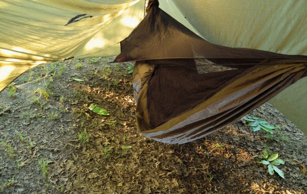 A camping hammock seen with a mosquito cover, as well as a rain tarp set up over the hammock for the ultimate in protection from the elements.